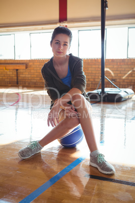 Portrait of confident woman sitting on basketball