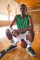 Portrait of teenage boy sitting on basketball