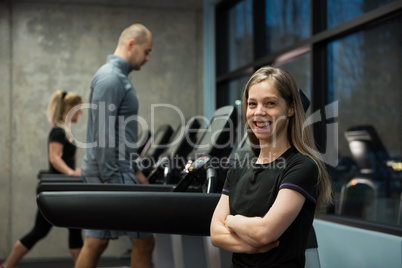 Smiling woman standing with people exercising on treadmill