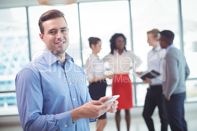 Smiling businessman using mobile phone with colleagues discussing in background