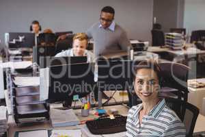 Smiling businesswoman sitting on chair with colleagues working at office