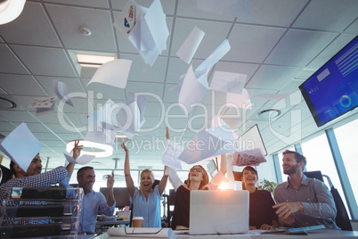 Cheerful business people tossing papers against ceiling
