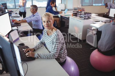 Portrait of businesswoman working at desk while sitting on exercise ball