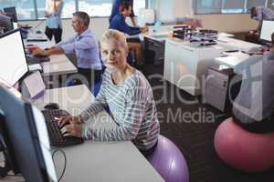 Portrait of businesswoman working at desk while sitting on exercise ball