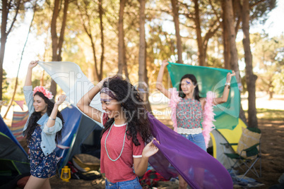 Happy young woman holding scarfs at campsite