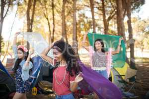 Happy young woman holding scarfs at campsite