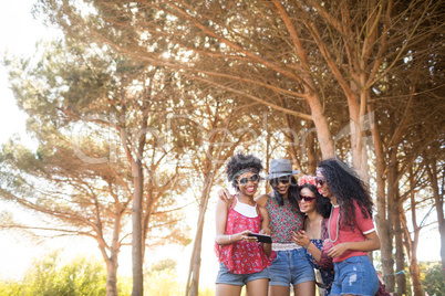 Smiling female friends using mobile phone against trees