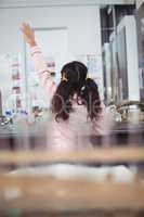 Rear view of elementary schoolgirl raising hand at science laboratory