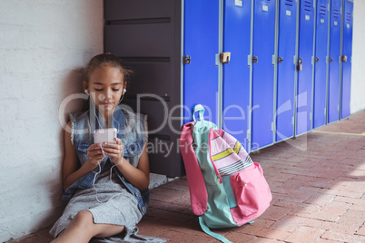 Elementary student listening music through headphones while using mobile phone