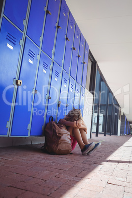 Full length of schoolgirl sitting by lockers