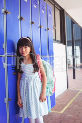 Portrait of elementary girl standing by lockers in corridor