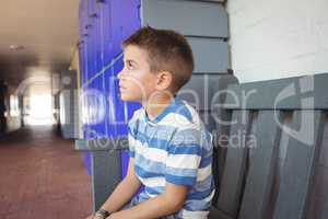 Thoughtful boy sitting on bench in corridor