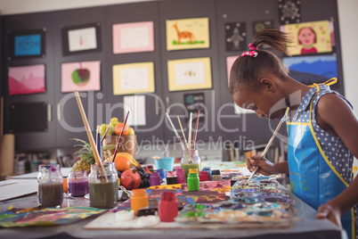 Side view of girl holding brush by color palettes on desk