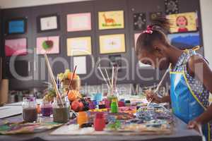 Side view of girl holding brush by color palettes on desk
