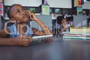 Thoughtful girl holding digital tablet in library