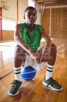 Portrait of teenage boy with hands clasped sitting on basketball