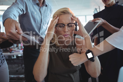 Frustrated businesswoman sitting amidst team holding technologies