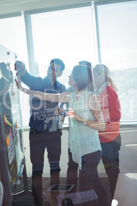 Business entrepreneurs seen through glass discussing over whiteboard