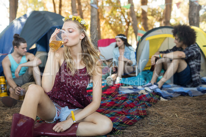Young woman drinking beer while sitting at campsite