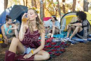 Young woman drinking beer while sitting at campsite
