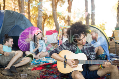 Young man playing guitar with friends sitting in background