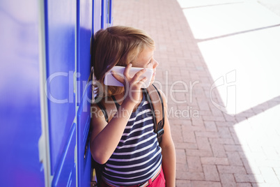 Schoolboy talking on mobile phone while standing by lockers in corridor