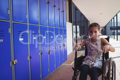 Portrait of schoolgirl sitting on wheelchair by lockers