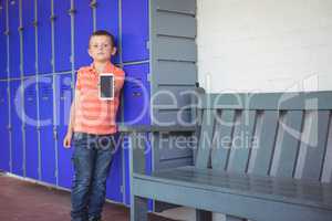 Portrait of boy showing mobile phone while leaning on lockers