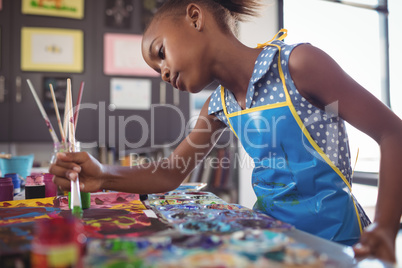 Focused elementary girl painting at desk