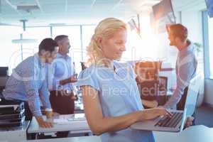 Businesswoman working on laptop with team discussing in background