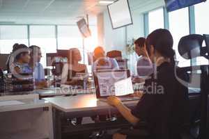 Businesswoman working on laptop while colleagues discussing at desk