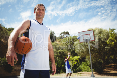 Portrait of man with basketball with friend playing in background