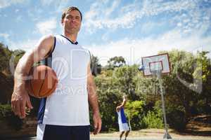 Portrait of man with basketball with friend playing in background