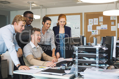 Colleagues standing by businessman working on computer in office