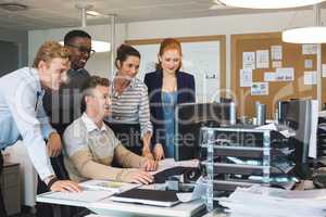 Colleagues standing by businessman working on computer in office