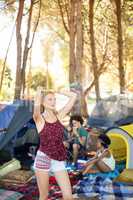 Happy young woman standing with arms raised at campsite