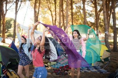 Happy female friends holding scarfs at campsite