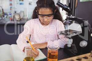 Elementary student writing in book by microscope at laboratory