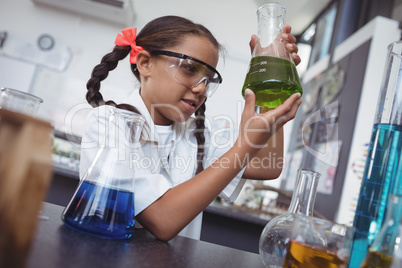 Elementary student examining green chemical in flask at laboratory