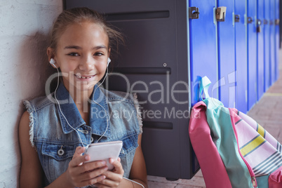 Portrait of elementary schoolgirl listening music through headphones by lockers