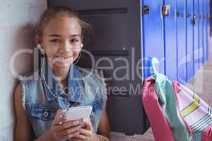 Portrait of elementary schoolgirl listening music through headphones by lockers