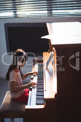 High angle side view of girl wearing headphones while practicing piano