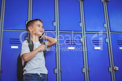 Happy boy talking on mobile phone against lockers