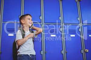 Happy boy talking on mobile phone against lockers