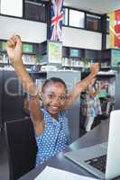 Cheerful girl with arms raised at desk in library