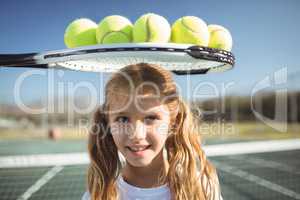 Smiling girl standing below tennis racket and balls