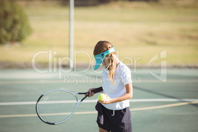 Girl holding tennis ball and racket on court