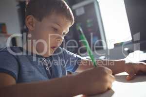 Boy writing in book on desk at classroom