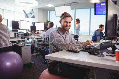 Portrait of young businessman working at desk while sitting on exercise ball