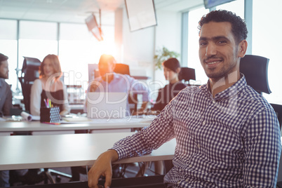 Businessman sitting at desk with colleagues in background